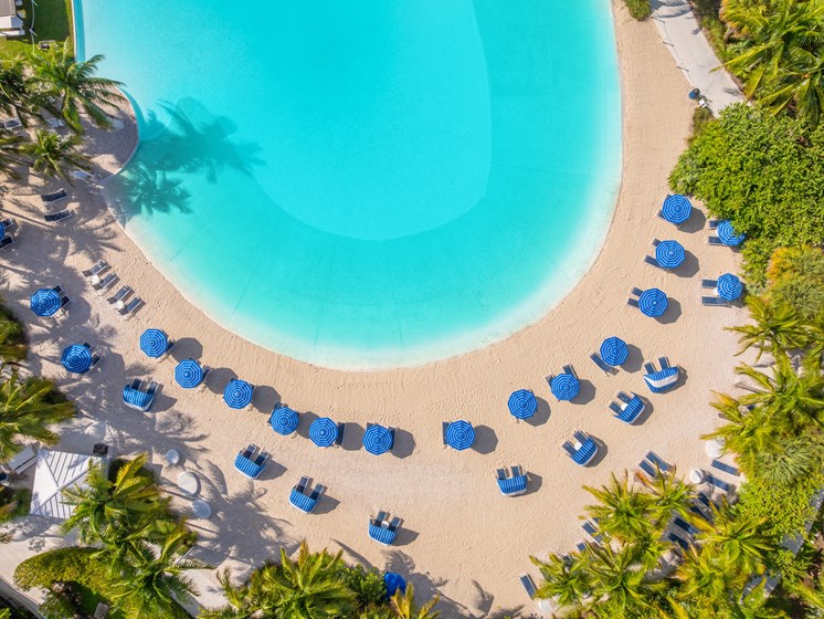 An aerial view of a beach with blue umbrellas and a swimming pool.